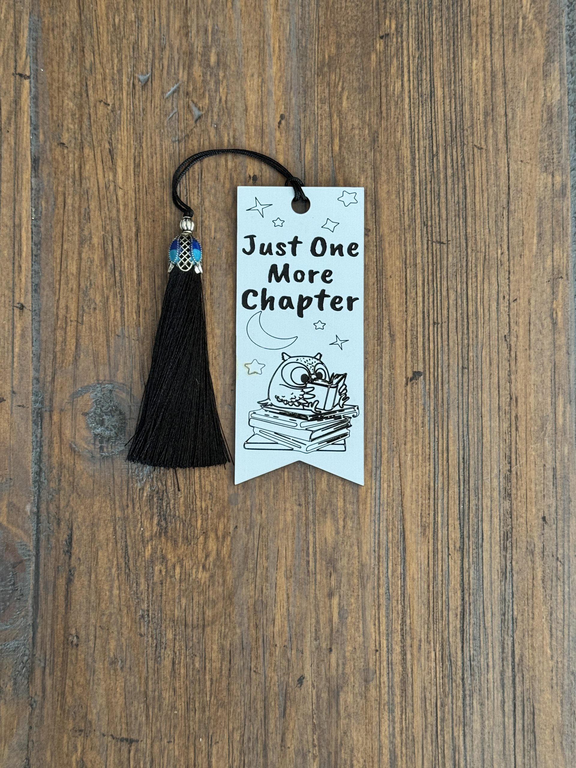 White acrylic bookmark with “Just One More Chapter” text, owl reading a book, moon and stars illustration, and black tassel